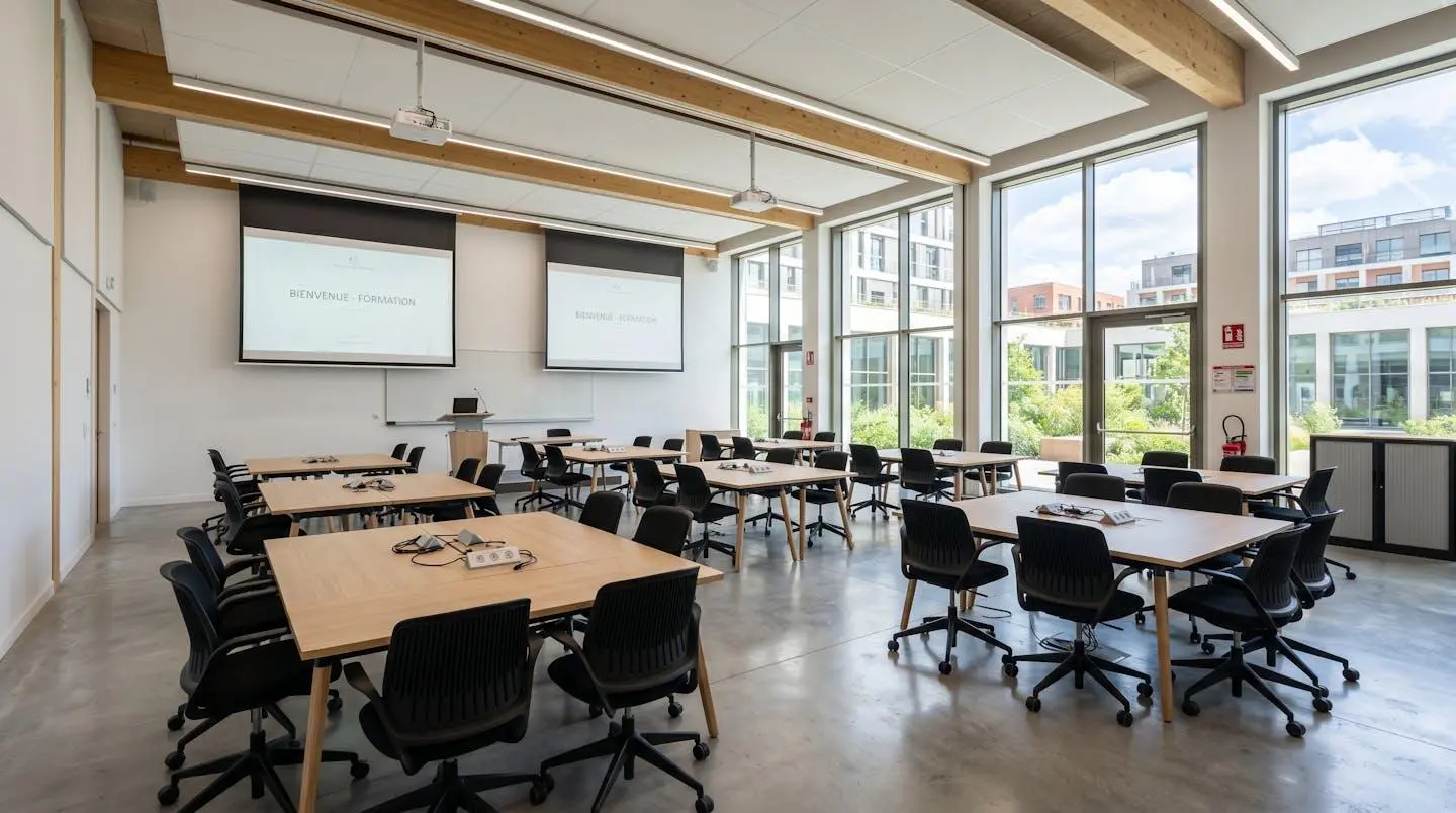 Salle de formation professionnelle moderne à Toulouse avec tables en îlots, écrans de projection et architecture européenne lumineuse, espace vide prêt à accueillir des apprenants
